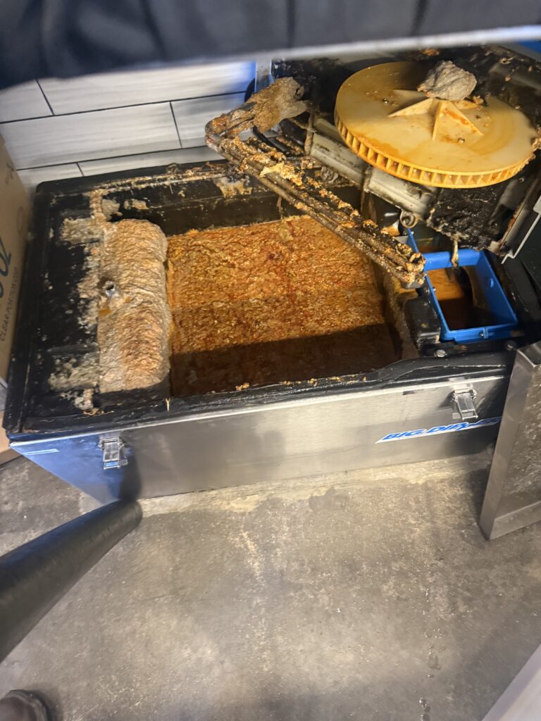 Professional team performing grease trap cleaning in Orange, removing fats, oils, and grease from a commercial kitchen grease management system.