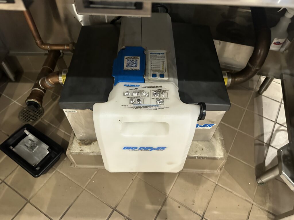 Grease trap under a restaurant sink in Anaheim, filled with accumulated fats, oils, and grease before cleaning.